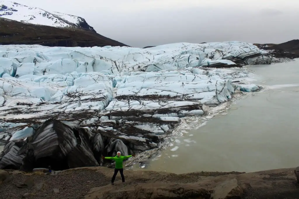 Gwen standing with arms spread wide in front of a glacier