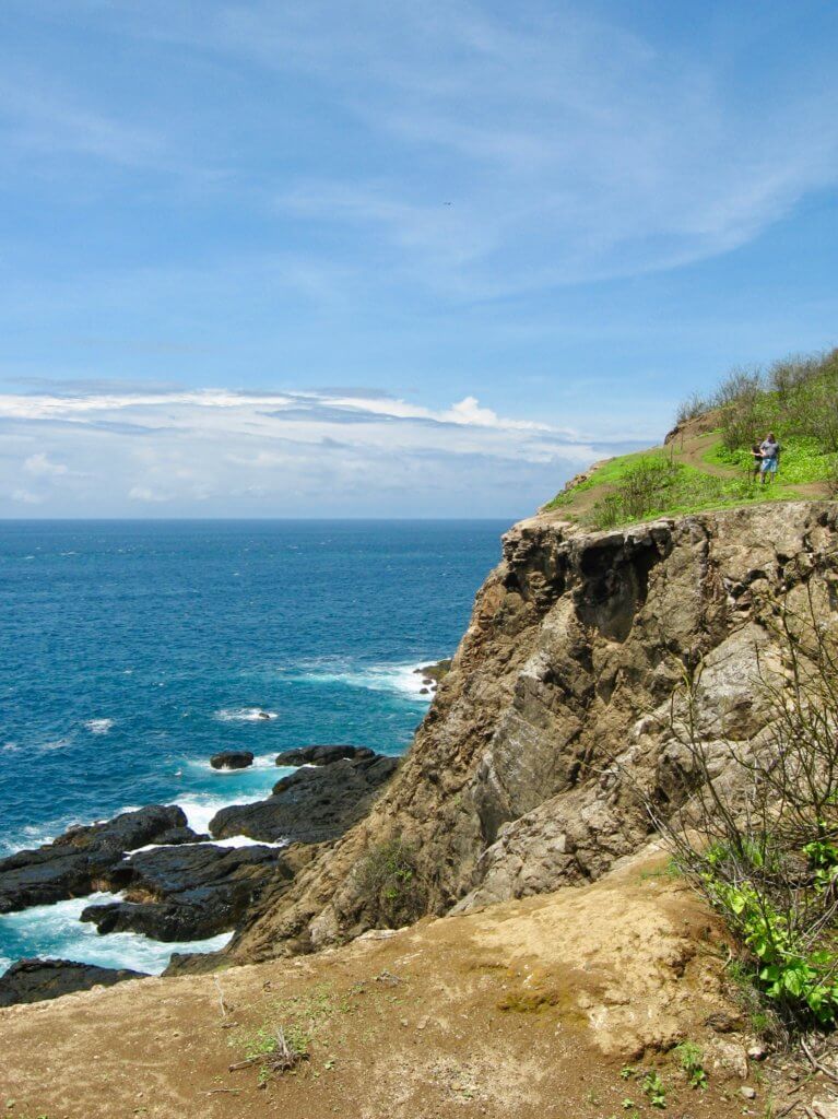 Brown cliff leading down to turquoise ocean with rocks and waves