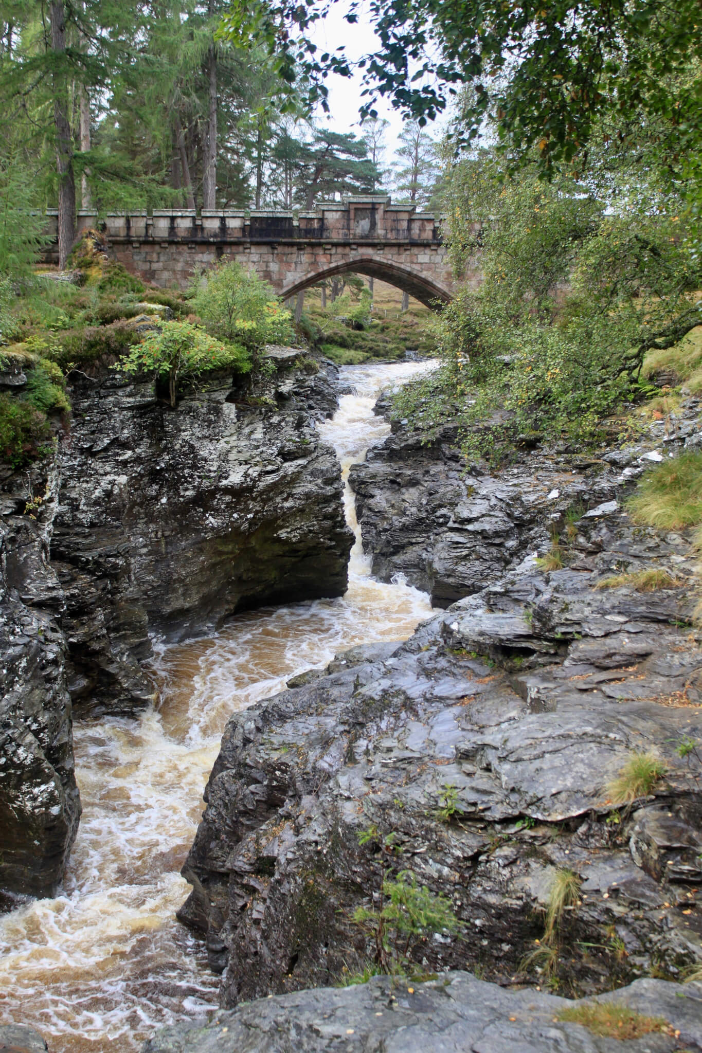 Stone bridge spanning canyon of black rocks and churning brown water. We added the Linn of Dee to our week in Scotland itinerary at the recommendation of our innkeepers.