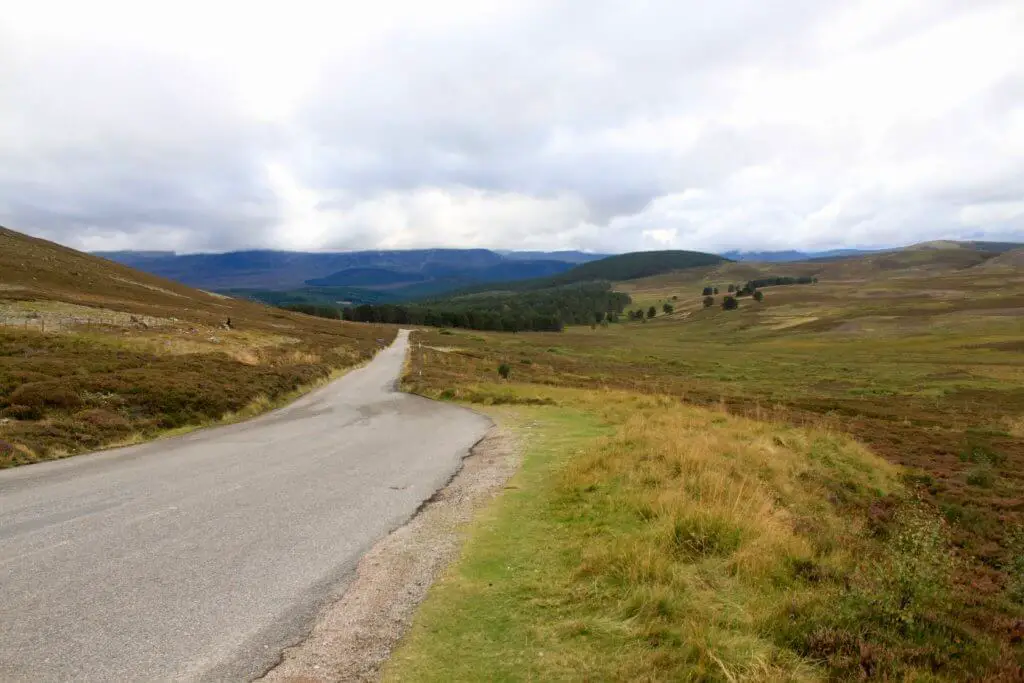 Narrow road winding through barren Highland hills. The Cairngorms are a great addition to a week in Scotland itinerary. 