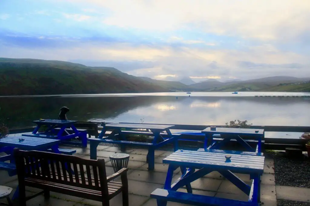Blue picnic tables in front of a loch at dawn