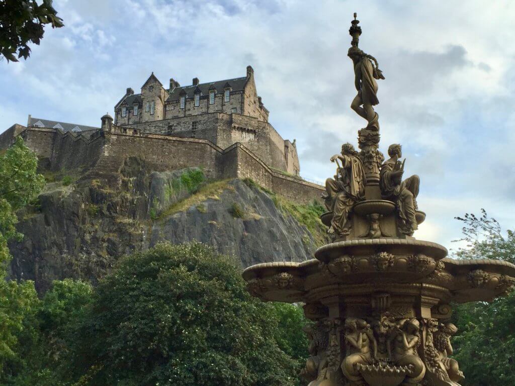 Edinburgh castle on a rocky hill behind a fountain. The castle was one of the most impressive stops on our itinerary for one week in Scotland.