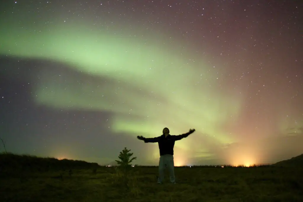 Max in silhouette with arms spread wide under the northern lights