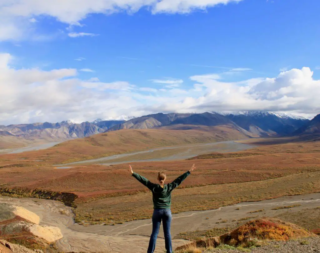 Gwen with arms spread wide in front of Polychrome Pass in Denali National Park