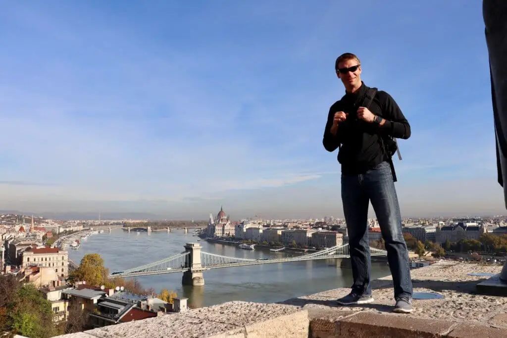 M in front of a panoramic vista of the Danube, with the Chain Bridge and Parliament Building in the distance