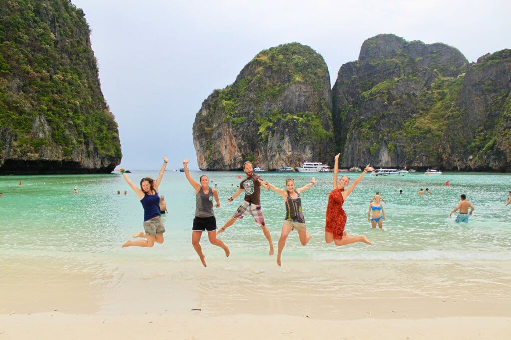 Five people jumping for joy in front of the karst formations and beautiful water of Maya Bay