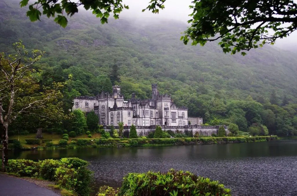 Kylemore Abbey along lake with misty forest around it