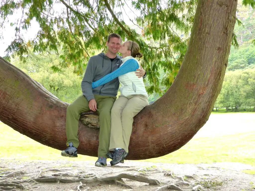 Gwen kissing M on the cheek as they sit on the huge bowed bough of a tree