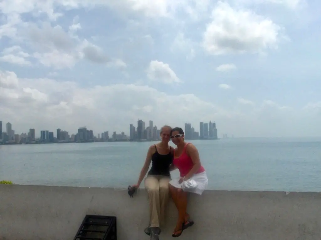 Gwen and Cristina sitting on a sea wall in front of Panama City skyline