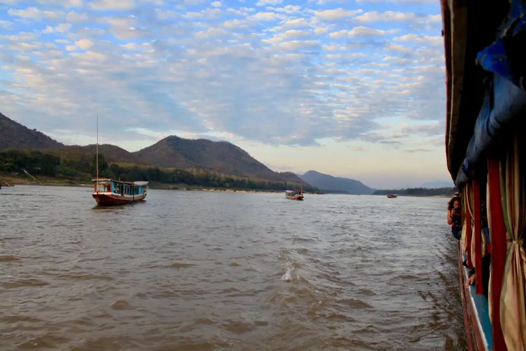 Longboats coming up behind as dusk falls and the sky is filled with color - the end of a beautiful Laos Mekong River Cruise