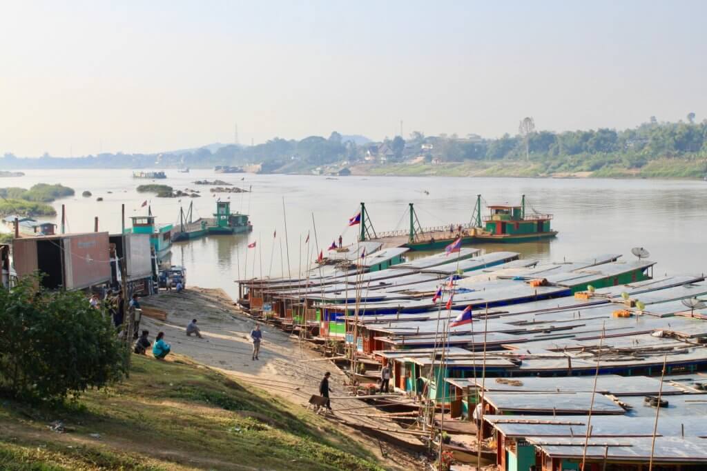 Numerous colorful longboats lined up side-by-side along the shoreline of the Mekong River