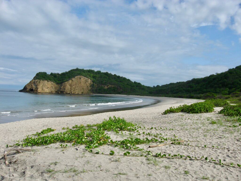 Half-moon-shaped stretch of empty beach with rocky cliffs at one end