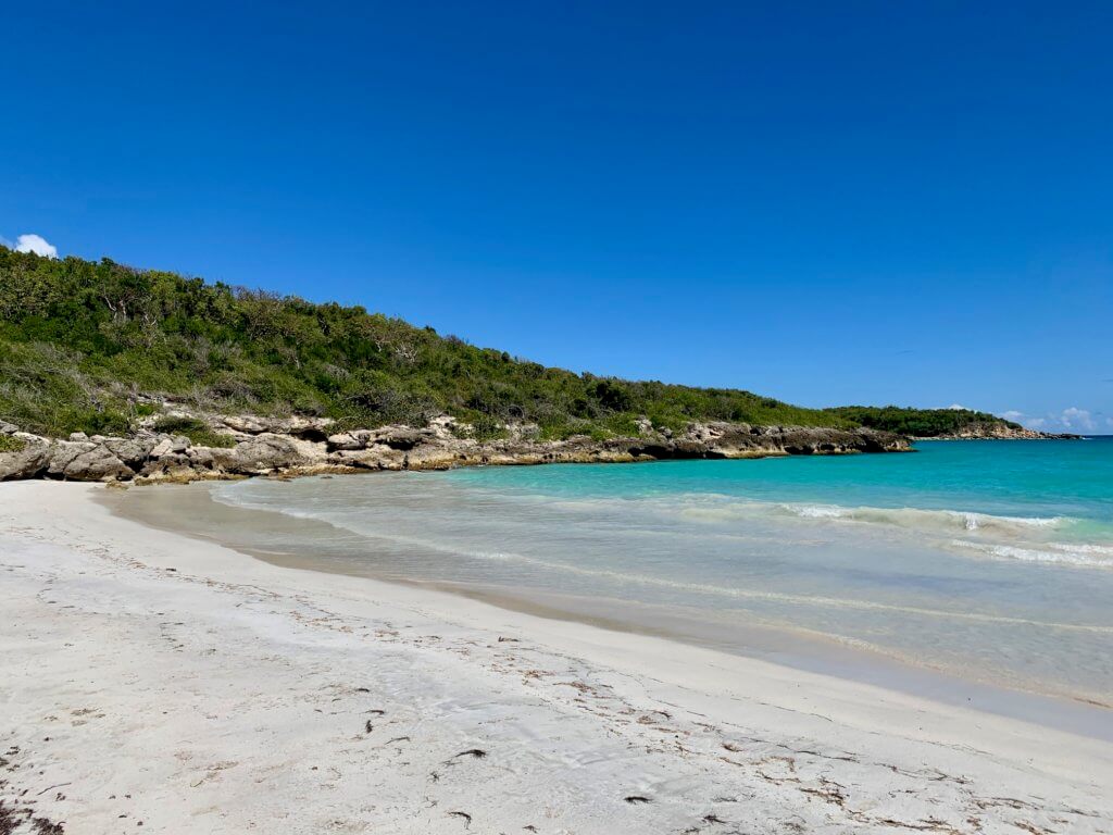 Rocks spilling onto white sand beach with teal water