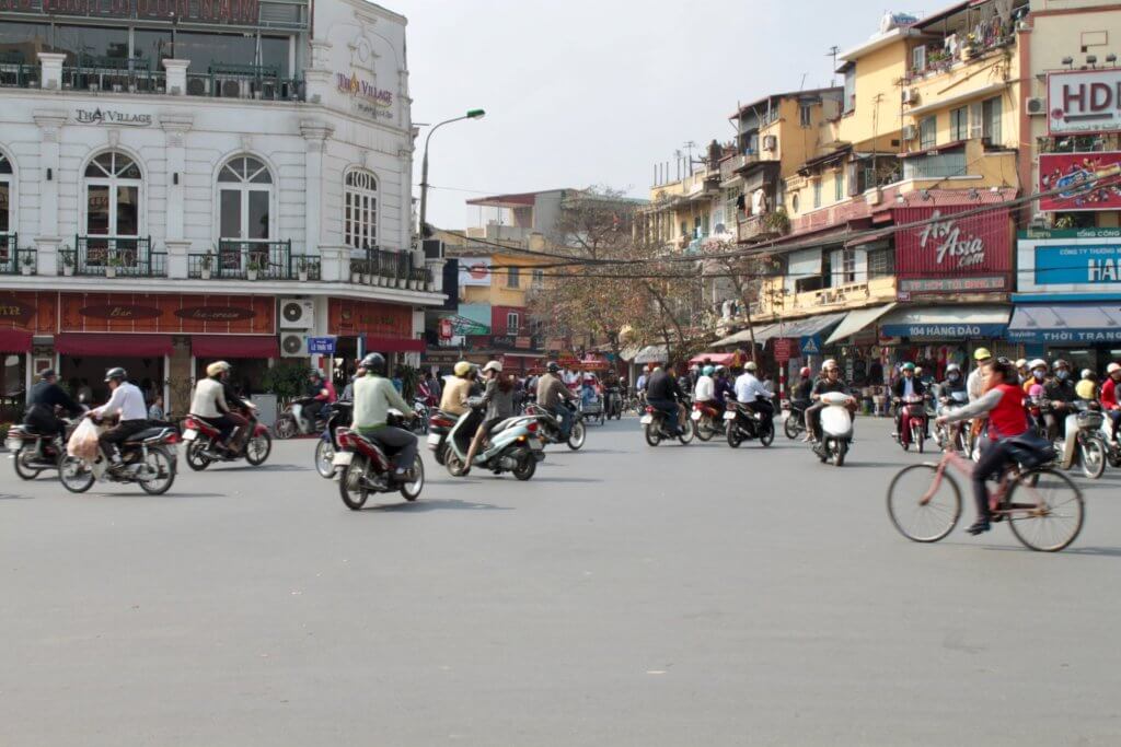 Motorbikes and bicycles traveling in all directions through an open square in Hanoi, Vietnam