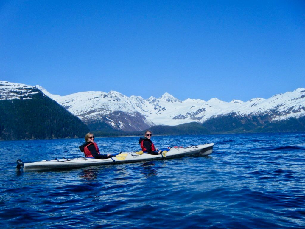 Gwen and a friend kayaking in front of snow-capped mountains