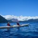 Gwen and a friend kayaking in front of snow-capped mountains