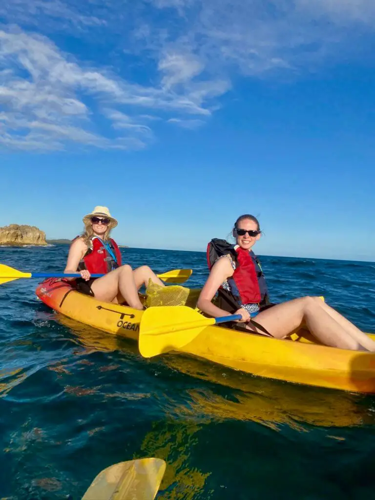 Brooke and Gwen smiling on a yellow kayak in the ocean