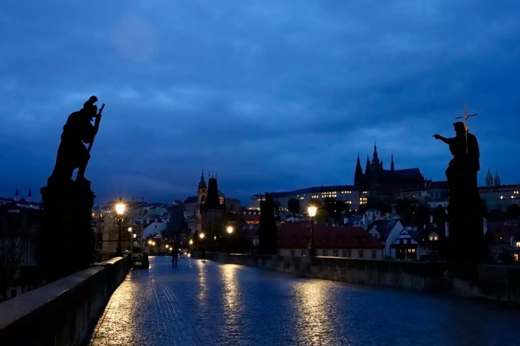 Pre-dawn on the Charles Bridge with silhouettes of statues and Prague Castle in the distance