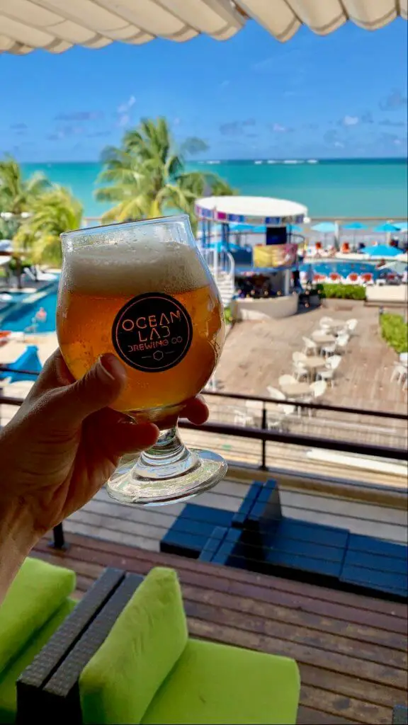 Glass of Ocean Lab beer being held in front of a view of the beach club