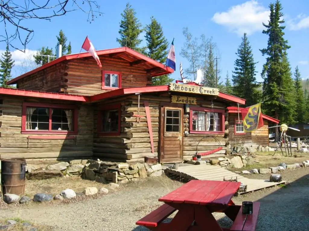 Red-roofed log cabin with "Moose Creek Lodge" sign - a worthy lunch stop on your Yukon itinerary