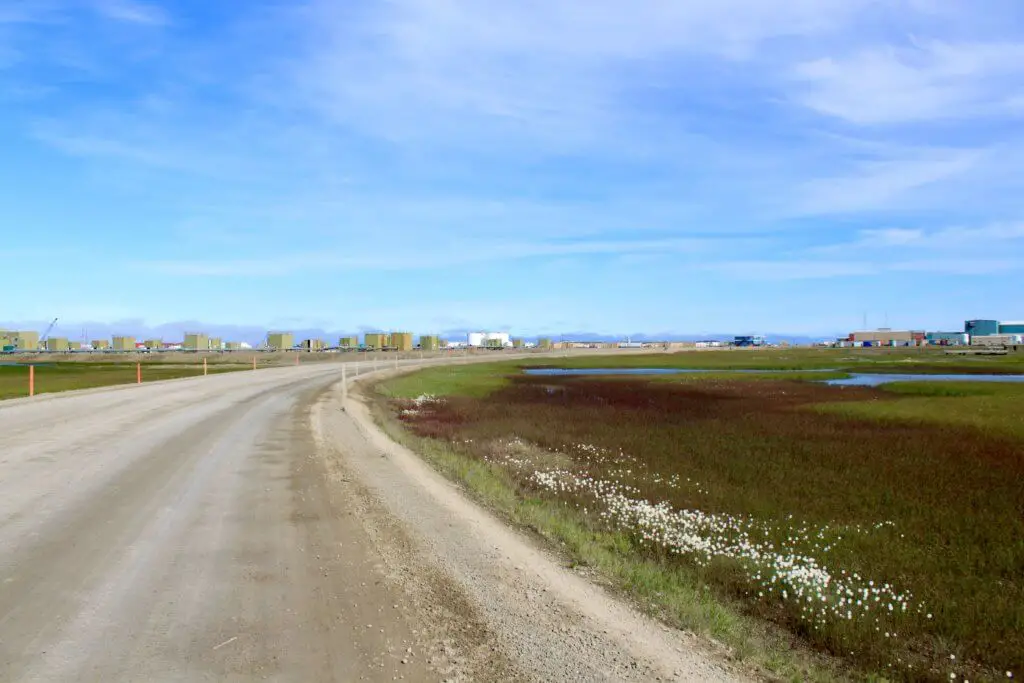 Dirt road flanked by oil buildings and storage containers in Prudhoe Bay