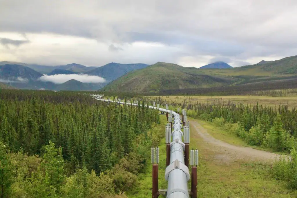 The Alaska Pipeline stretching off into the distance through evergreen forests and mountains 