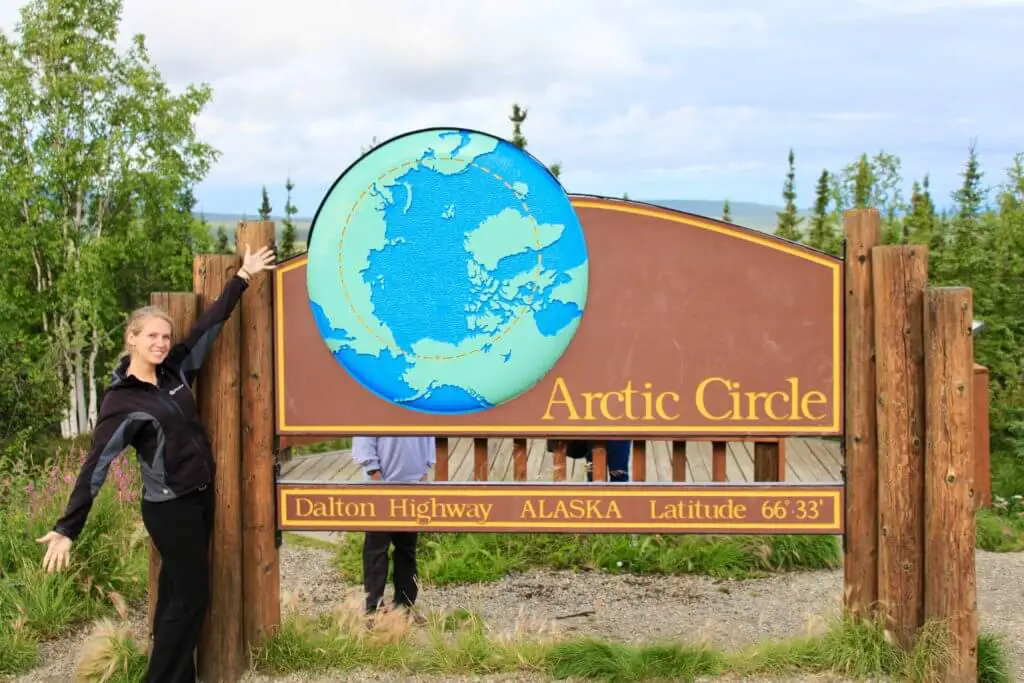 Gwen with arms spread wide at a sign marking the Arctic Circle