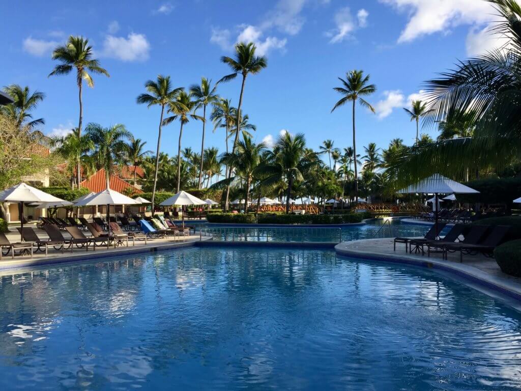 The pool area of an all-inclusive resort in the Dominican Republic, ringed by chairs, umbrellas, and palm trees.