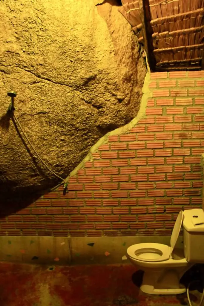 Giant boulder with showerhead hanging off and toilet beside