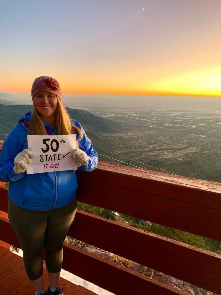 Molly holding a paper sign noting her 50th state in front of an Albuquerque sunset