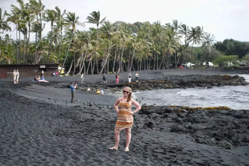 Molly standing on a black sand beach with palm trees behind