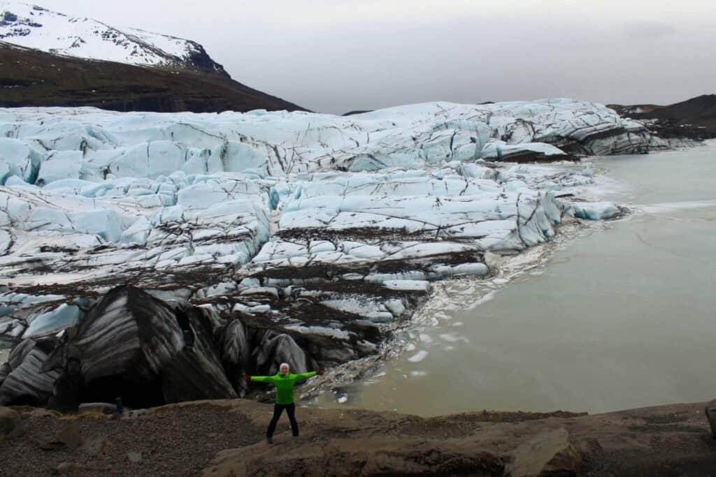 Gwen standing with arms spread wide in front of a glacier