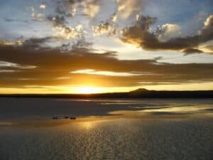 Sunset reflecting off shallow water with clouds, colorful sky, and mountain silhouettes